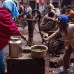 A boy helps a woman fill her pots with water onthe street sof Paharganj in Delhi, India. Photo by Pete Bracey.